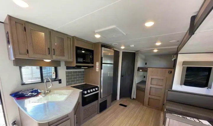 Spacious RV rental interior featuring a modern kitchen with microwave, stove, sink, refrigerator, plus dinette and bunk beds.. Other Hideout 2021
