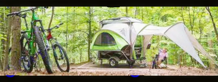 RV rental for nature lovers! Trailer with tent/awning, bikes, and a person relaxing in a forest campsite.. Other Other 2018