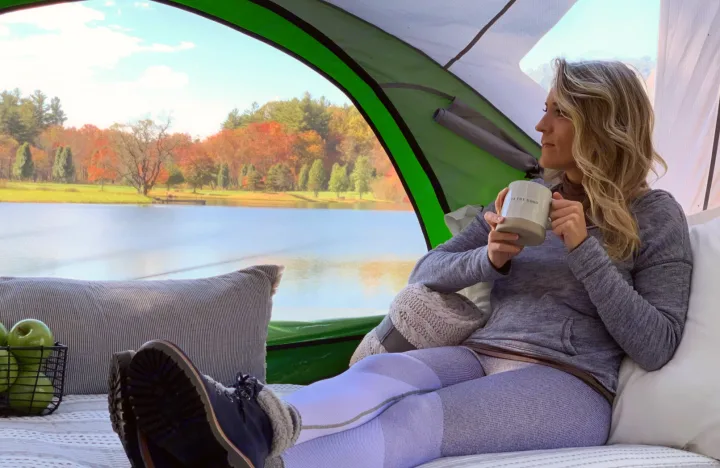 A woman relaxing in an RV rental setup, enjoying coffee & breathtaking autumn lake views from a cozy tent.. Other Other 2018