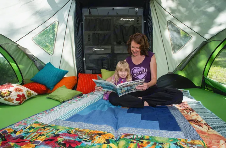 Cozy family moment inside an RV rental. A mother and child read a book surrounded by colorful pillows and blankets.. Other Other 2018