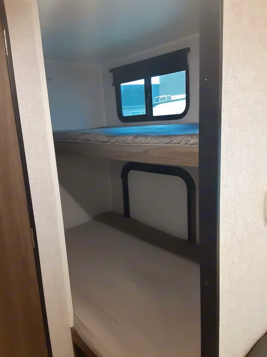 RV rental bunk beds. View from a lower bunk shows the top bunk's support structure and window, perfect for compact sleeping.. Dutchmen Kodiak 2021