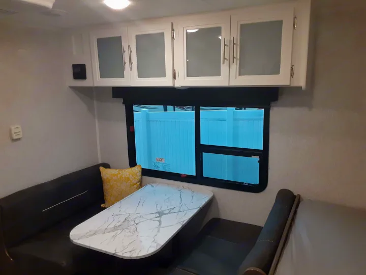 Modern RV rental dinette with white cabinets, comfortable seating, and a marble-look table. Perfect compact living space.. Dutchmen Kodiak 2021