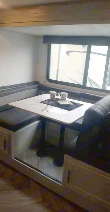 Step into this RV rental's dinette, offering cozy booth seating, a table, and a window view.. Forest River Wildwood 2021