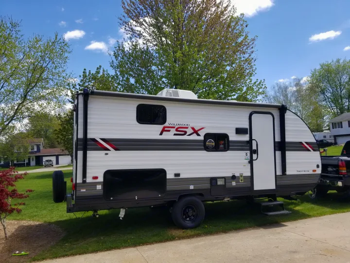 This white & grey Wildwood FSX travel trailer, perfect for an rv rental, is parked on a sunny lawn.. Forest River Wildwood 2021