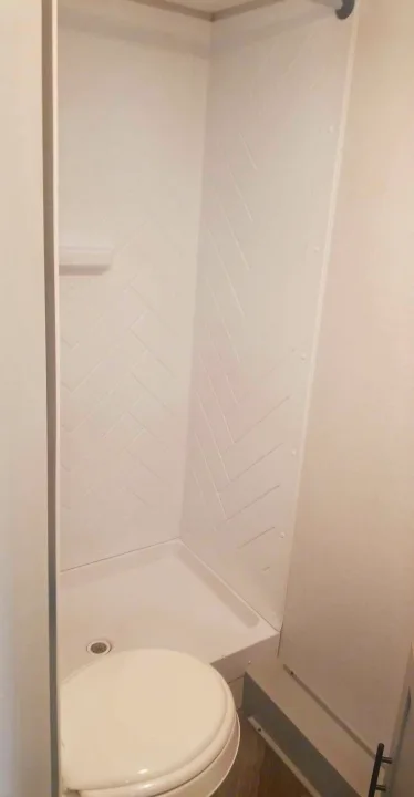 Modern RV rental bathroom: white herringbone shower, compact design, and a clean toilet.. Forest River Wildwood 2021