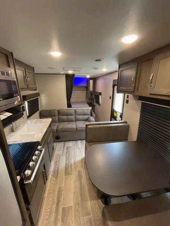 Modern RV rental interior with kitchen (sink, stove, microwave), sofa seating, and dining booth. Features wood-look floors.. Jayco Jay Flight 2021