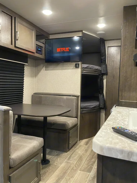 Cozy RV rental interior with a dinette, bunk beds, and a TV displaying Netflix, offering comfortable living space.. Jayco Jay Flight 2021