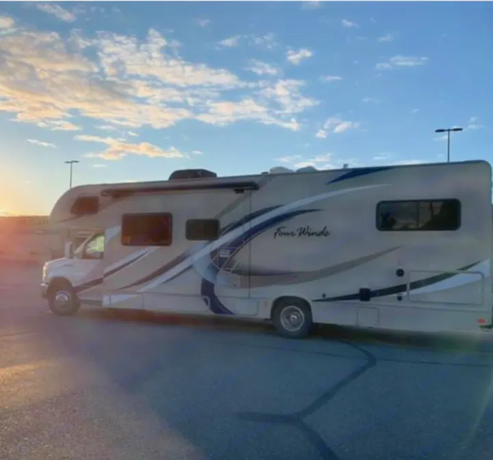 This tan Four Winds RV rental, adorned with dynamic graphics, is parked at sunset, ready for your road trip adventure.. Thor Motor Coach Four Winds 2019