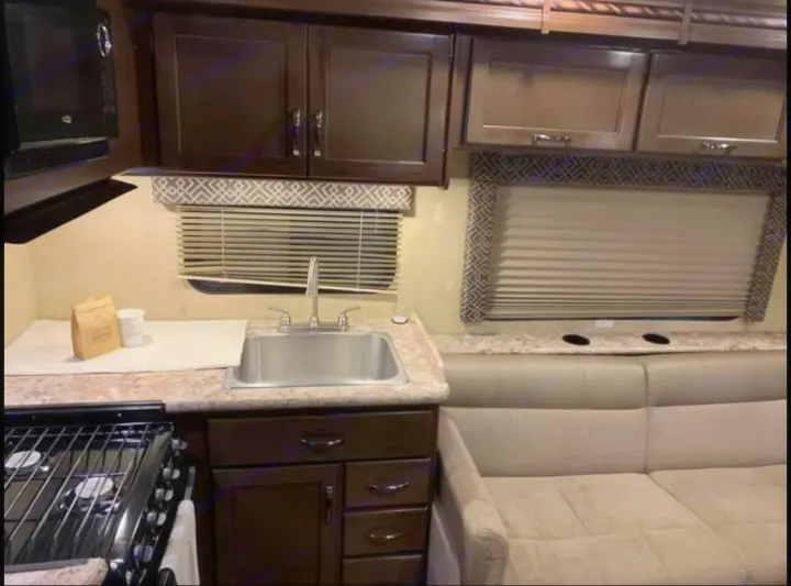 RV rental interior: a compact kitchen with sink & stove, plus a comfy dinette with window. Dark cabinets & light surfaces.. Thor Motor Coach Four Winds 2019