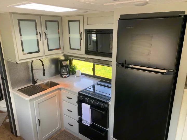Compact RV rental kitchen featuring light cabinets, a stainless sink, and sleek black appliances like the fridge and stove.. Forest River Vibe 2021