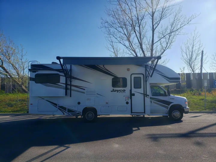 White Jayco motorhome RV rental, with its awning extended, parked for a sunny travel adventure.. Jayco REDHAWK 2020