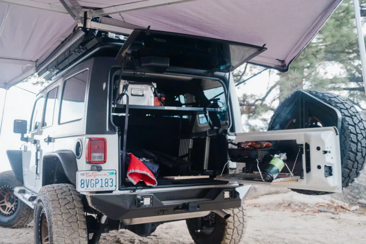 An organized Jeep with a deployed awning and tailgate kitchen, ideal for off-road camping or compact RV rental trips.. Jeep Wrangler Rubicon 2017