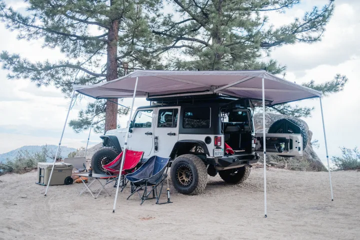 White Jeep Wrangler outfitted for overlanding with an awning, chairs, and cooler on dirt. Ideal rv rental for adventure!. Jeep Wrangler Rubicon 2017
