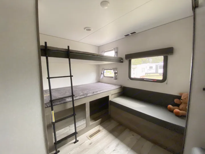 Cozy RV rental interior showing bunk beds with ladder, a long bench seat, and windows with outdoor views.. Sportsmen LE 2021