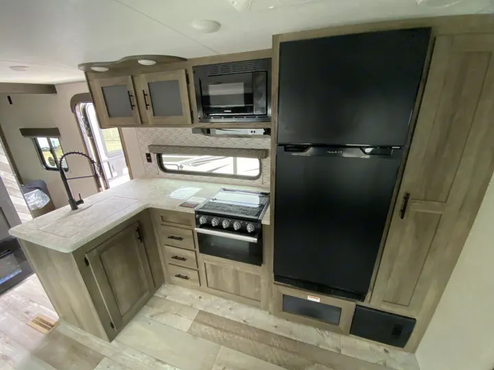 Modern RV rental kitchen with black fridge, microwave, stove, sink, and ample counter space for comfortable travels.. Sportsmen LE 2021