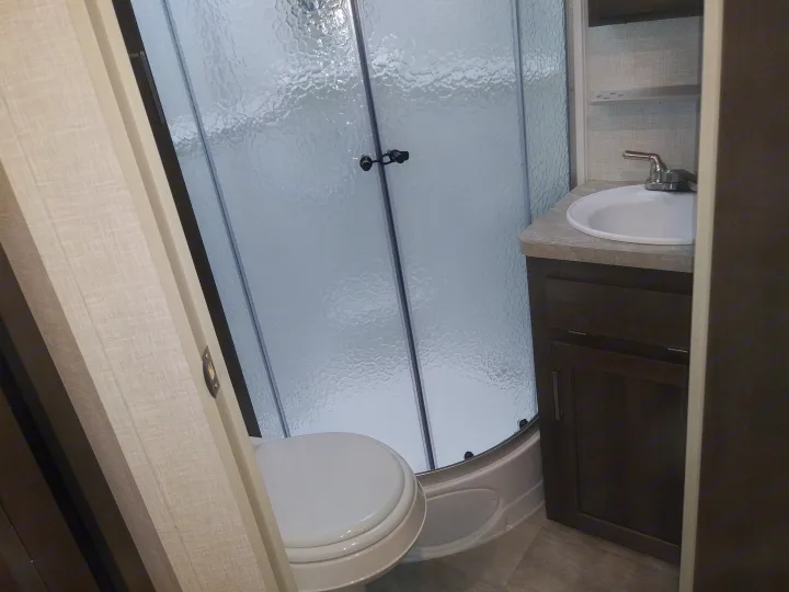 Compact RV rental bathroom with a white toilet, frosted glass shower, and vanity sink, showcasing practical use of space.. Forest River Rockwood Mini Lite 2021