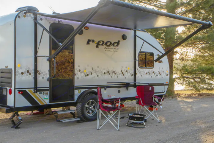 Relaxing at a scenic campsite with an r-pod travel trailer, awning extended, chairs, and fire pit. Perfect for your next RV rental adventure.. Forest River R-Pod 2021