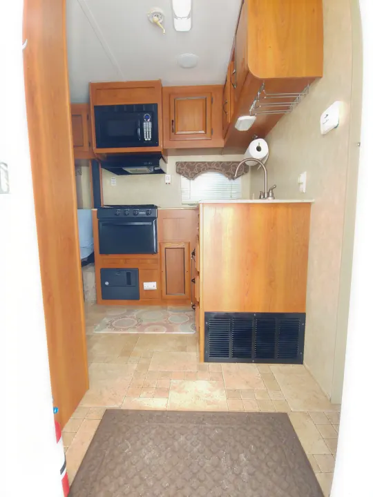 This RV rental features a clean kitchen with microwave, stove, and sink. Tiled flooring with a rug leads through the functional space.. Coachmen Catalina 2011