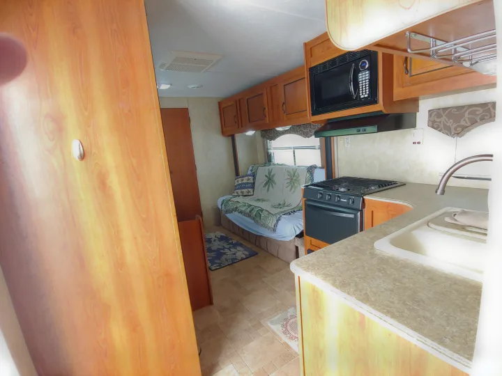 Inside this RV rental: full kitchen with microwave, stove, and sink; cozy living space with sofa, window, and overhead cabinets.. Coachmen Catalina 2011