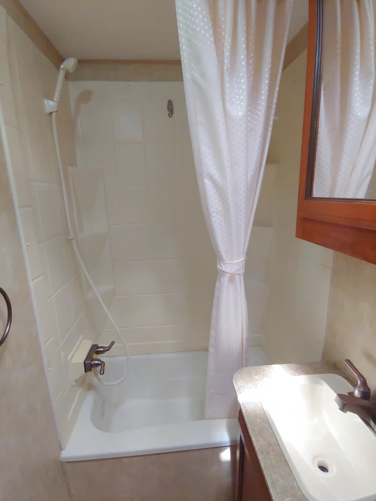 RV rental bathroom: compact tub with handheld shower, light patterned curtain, and vanity sink, maximizing space.. Coachmen Catalina 2011
