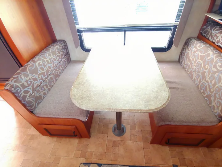 Bright RV rental dinette showing a table, comfortable patterned benches, and a large window. Ideal for travelers.. Coachmen Catalina 2011