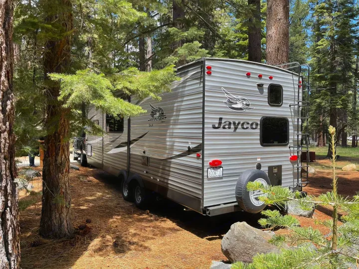Grey Jayco travel trailer at a sunny forest campsite. Explore nature with an rv rental like this!. Jayco Jay Flight 2021