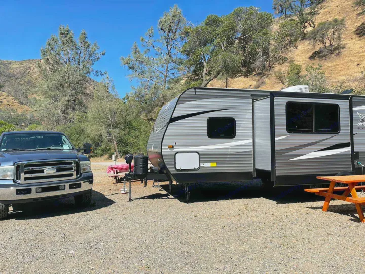 Scenic rv rental setup: A pickup truck and travel trailer at a gravel campsite with picnic tables.. Jayco Jay Flight 2021