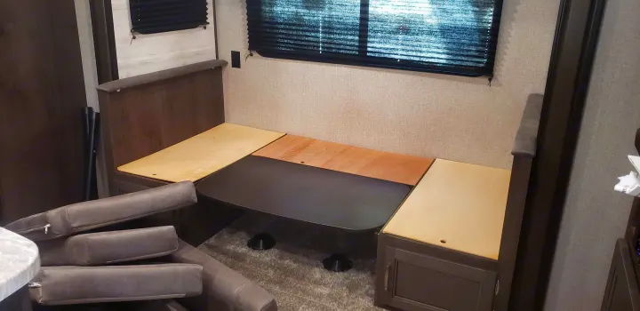 RV rental dinette with lowered table and removed cushions, forming a bed base. Interior shows textured walls and a window.. Jayco Jay Flight 2021