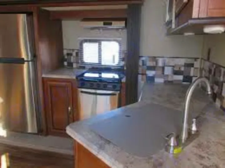 This RV rental kitchen features a stainless steel fridge, stove, and sink, with a checkered backsplash and wood cabinets.. Forest River Vibe 2016