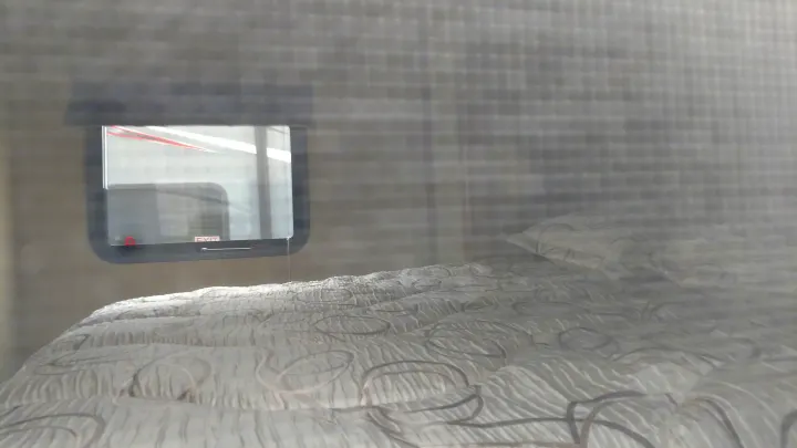 Inside an RV rental: a comfortable bed with a textured comforter and a window showing a reflected "EXIT" sign.. Forest River Vibe 2016