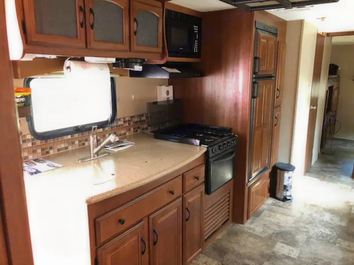 RV rental kitchen: a modern travel trailer interior with wood cabinets, sink, stove, microwave, and fridge.. Coachmen 310 BHDS 2015