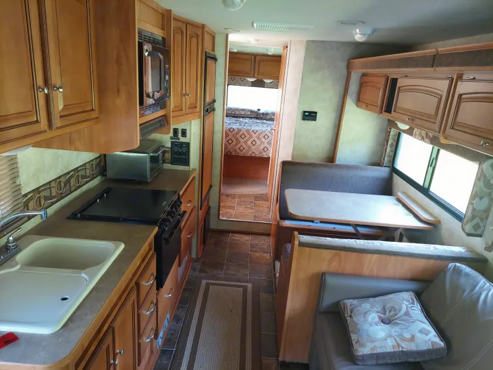 Spacious RV rental interior featuring a well-equipped kitchen, comfortable dining booth, and inviting bedroom.. Winnebago Access 2011