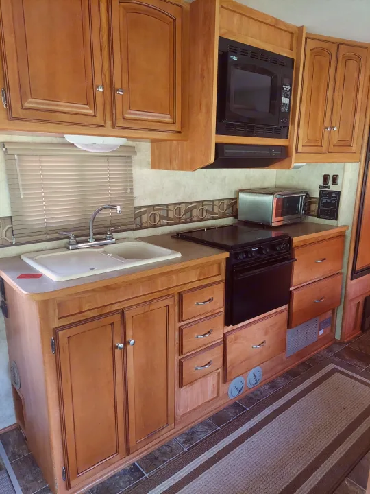 RV rental kitchen featuring light wood cabinets, a double sink, built-in microwave, stove, and a toaster oven.. Winnebago Access 2011