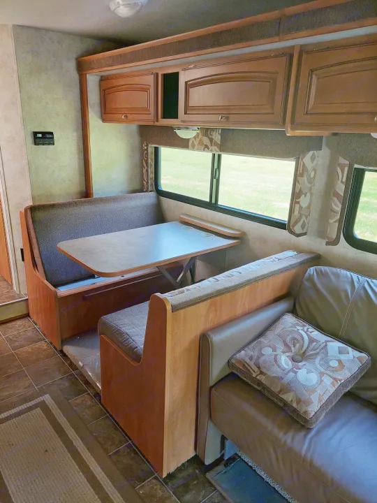 RV rental interior: a dinette with bench seating, large window to a green field, and brown sofa. Ready for travel.. Winnebago Access 2011