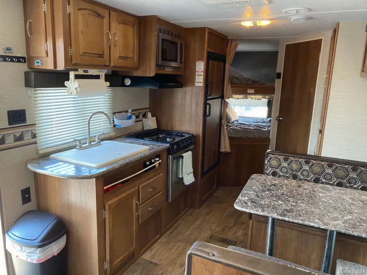 This RV rental features a full view of a modern RV interior, showing a compact kitchen, dining booth, and bunk bedroom.. Keystone Springdale 2016