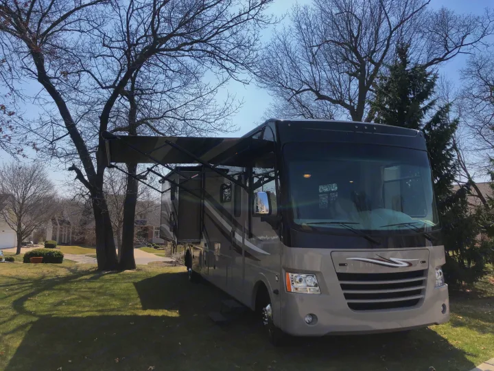 A grey RV rental, with its awning extended, is parked on a grassy lawn under a clear blue sky.. Coachmen Mirada 35BH 2016
