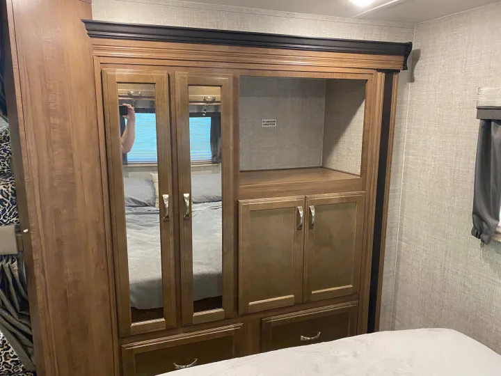 RV rental bedroom featuring a large wooden wardrobe with mirrored doors, a TV shelf, and lower storage cabinets.. Gulf Stream Conquest 2019