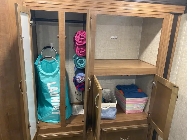 Organized RV rental cabinet: laundry bag, rolled towels, and storage bins. Includes a labeled TV backer area.. Gulf Stream Conquest 2019
