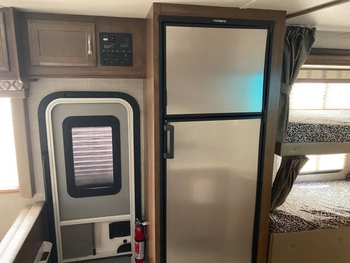 Experience an RV rental interior featuring a Dometic fridge, bunk beds with leopard print, control panel, and entry door with fire extinguisher.. Gulf Stream Conquest 2019