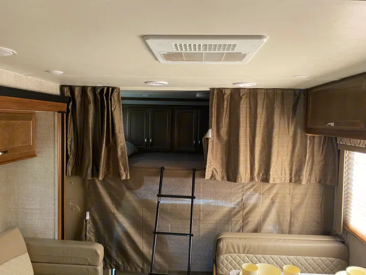 An RV rental's interior features a neatly made bunk bed accessible by a ladder, with privacy curtains and ceiling AC.. Gulf Stream Conquest 2019