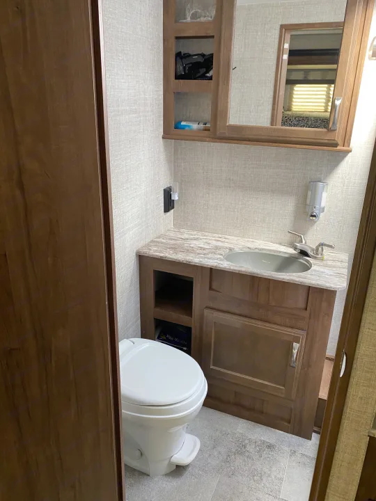 This RV rental's compact bathroom features a modern toilet, sink vanity, mirrored cabinet, and convenient storage.. Gulf Stream Conquest 2019