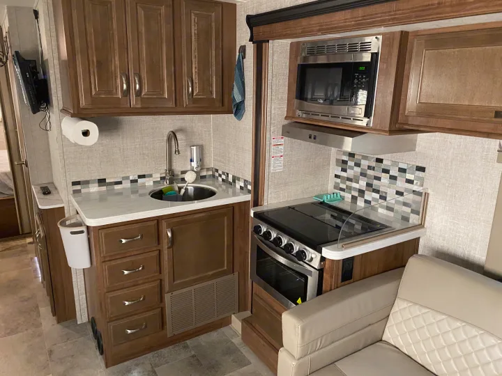 Inside an RV rental: a well-equipped kitchen with sink, microwave, and stove, next to a comfortable living area sofa.. Gulf Stream Conquest 2019