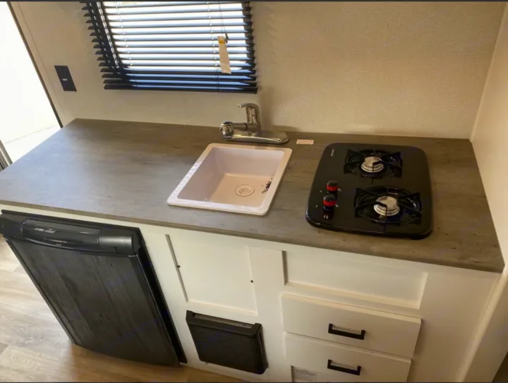 This RV rental kitchenette features a compact sink, 2-burner stove, fridge, and ample counter space for travelers.. keystone Hideout 2021