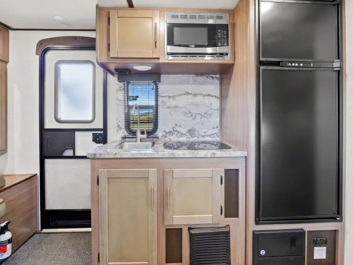 Compact RV rental kitchen features a sink, stovetop, microwave, and refrigerator, ideal for travel adventures.. Crossroads Sunset Trail Super Lite 2021