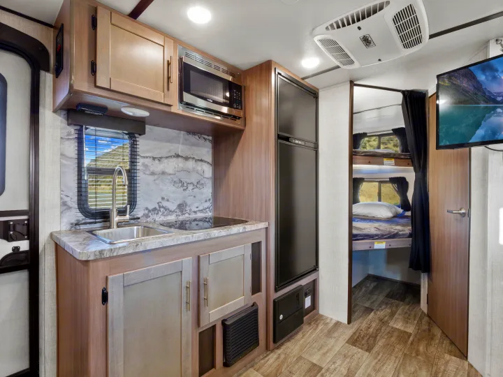 Compact RV rental interior featuring a modern kitchen with sink, microwave, fridge, and cozy bunk beds.. Crossroads Sunset Trail Super Lite 2021