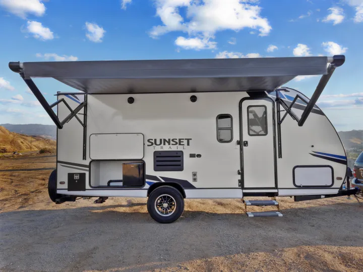 White "Sunset Trail" travel trailer RV with extended gray awning & open storage, ready for rv rental adventures.. Crossroads Sunset Trail Super Lite 2021