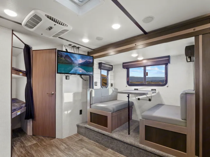 Spacious RV rental interior featuring a cozy dinette, wall-mounted TV, and bunk beds with privacy curtain for comfortable travel.. Crossroads Sunset Trail Super Lite 2021