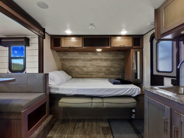 Spacious RV rental interior features a cozy bed, dining booth, kitchen, and scenic window views.. Crossroads Sunset Trail Super Lite 2021