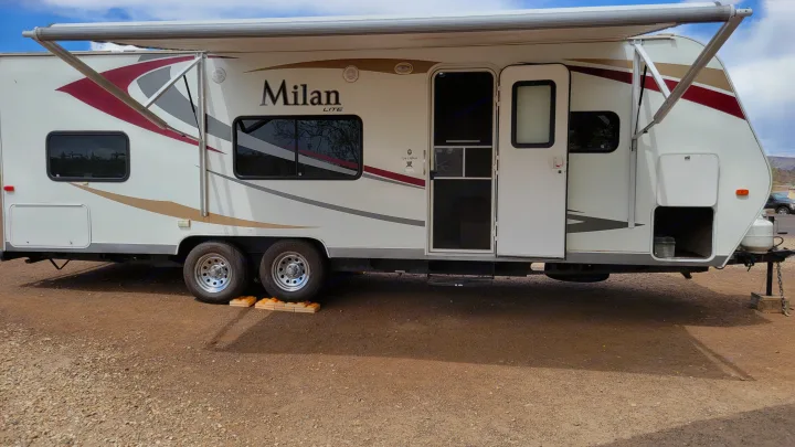 White Milan LITE RV rental parked on gravel with its awning extended and main door open.. Eclipse Recreational Vehicles Milan 2013