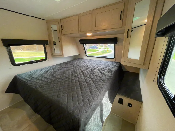 RV rental bedroom: a comfortable space with a quilted bed, large windows, and light-colored overhead storage.. Coachmen Apex 2021